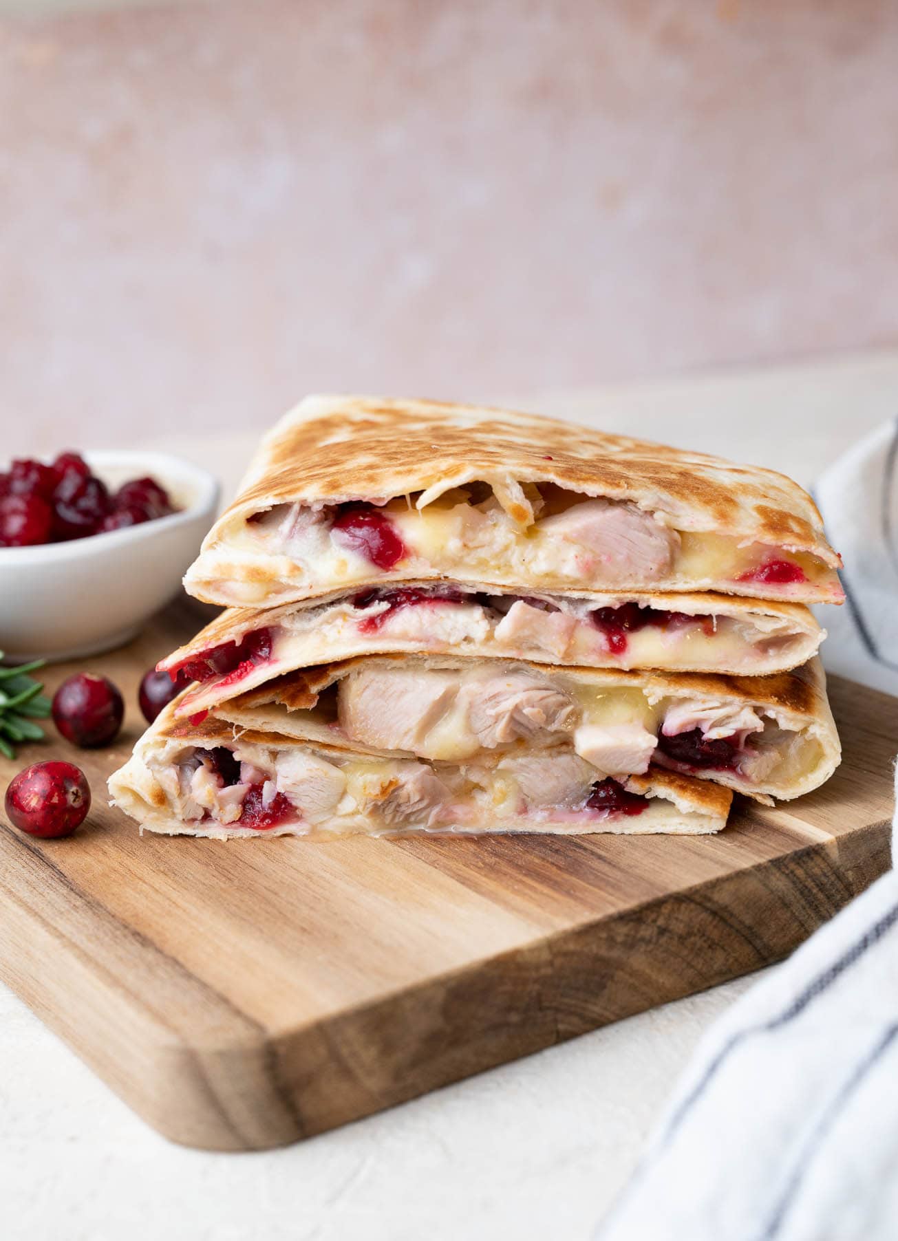 turkey and cranberry quesadilla on a wooden board with a bowl of cranberries