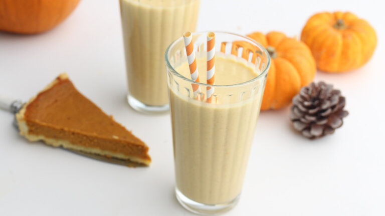 a glass of pumpkin pie milkshake with 2 straws, a piece of pie, small pumpkins and a pinecone