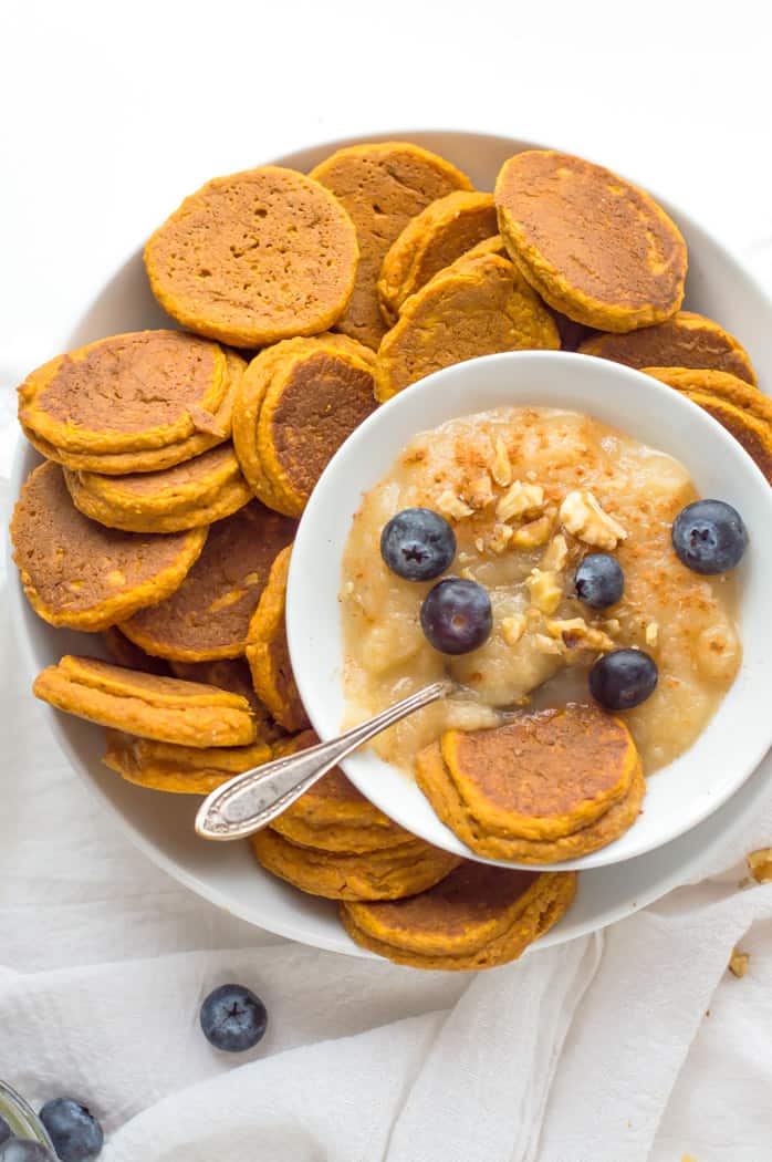 a plate of sweet potato pancakes next to a bowl of oatmeal and fruit